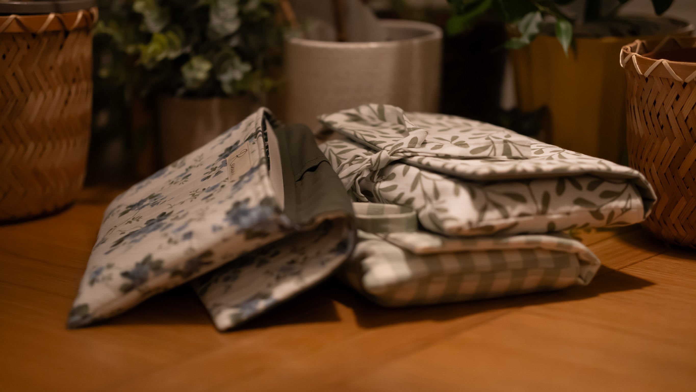 A stack of fabric book sleeves on a wooden surface with plants in the background