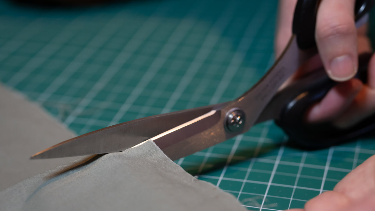 Scissors cutting green fabric on a green cutting mat