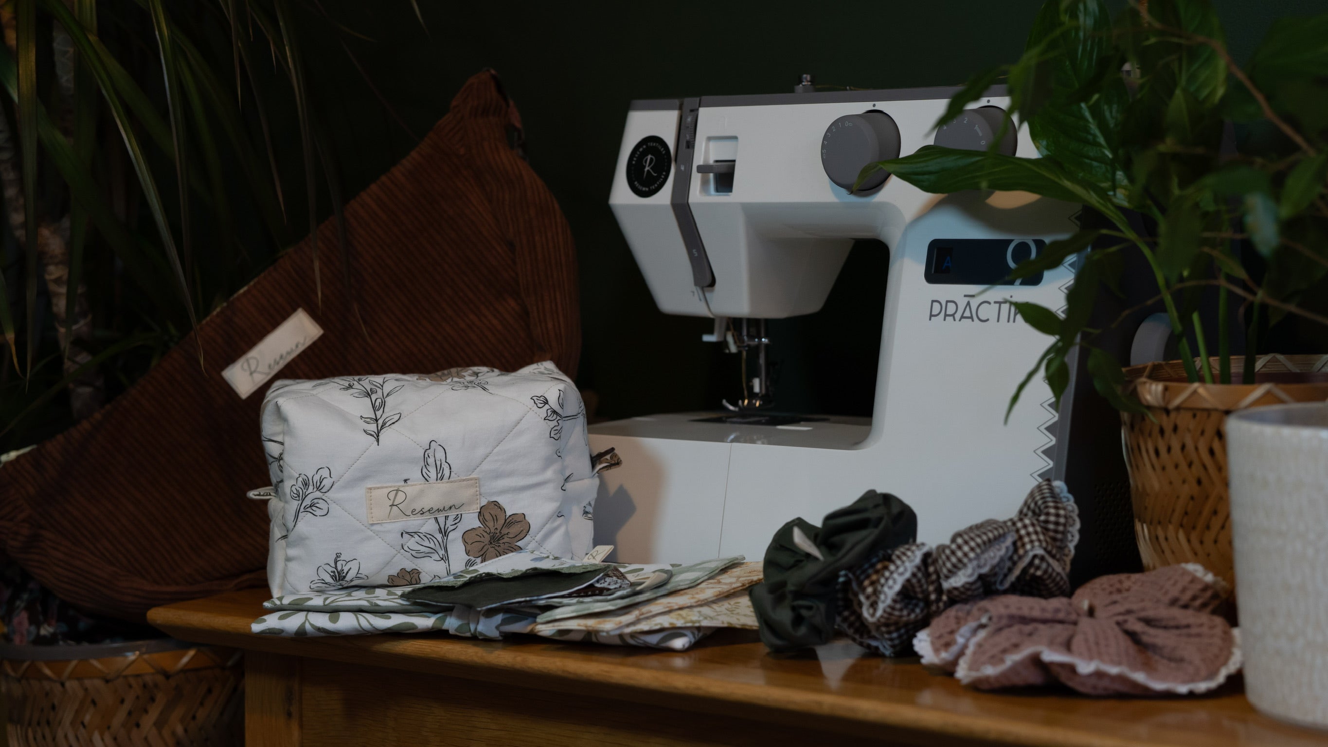 Sewing machine on a table with handmade bags, bookmarks and scrunchies on a wooden table and a plant in the background