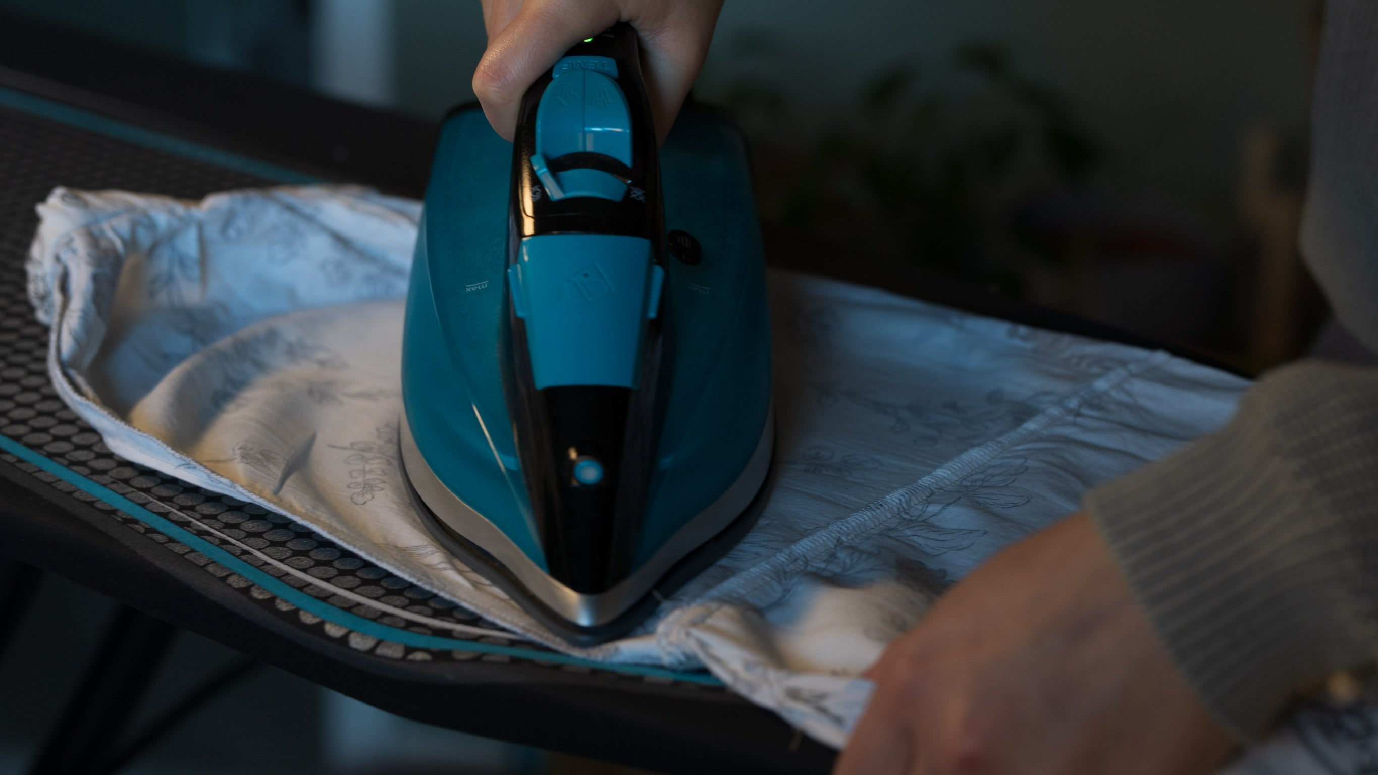 Person ironing a garment on a table with a blue iron.