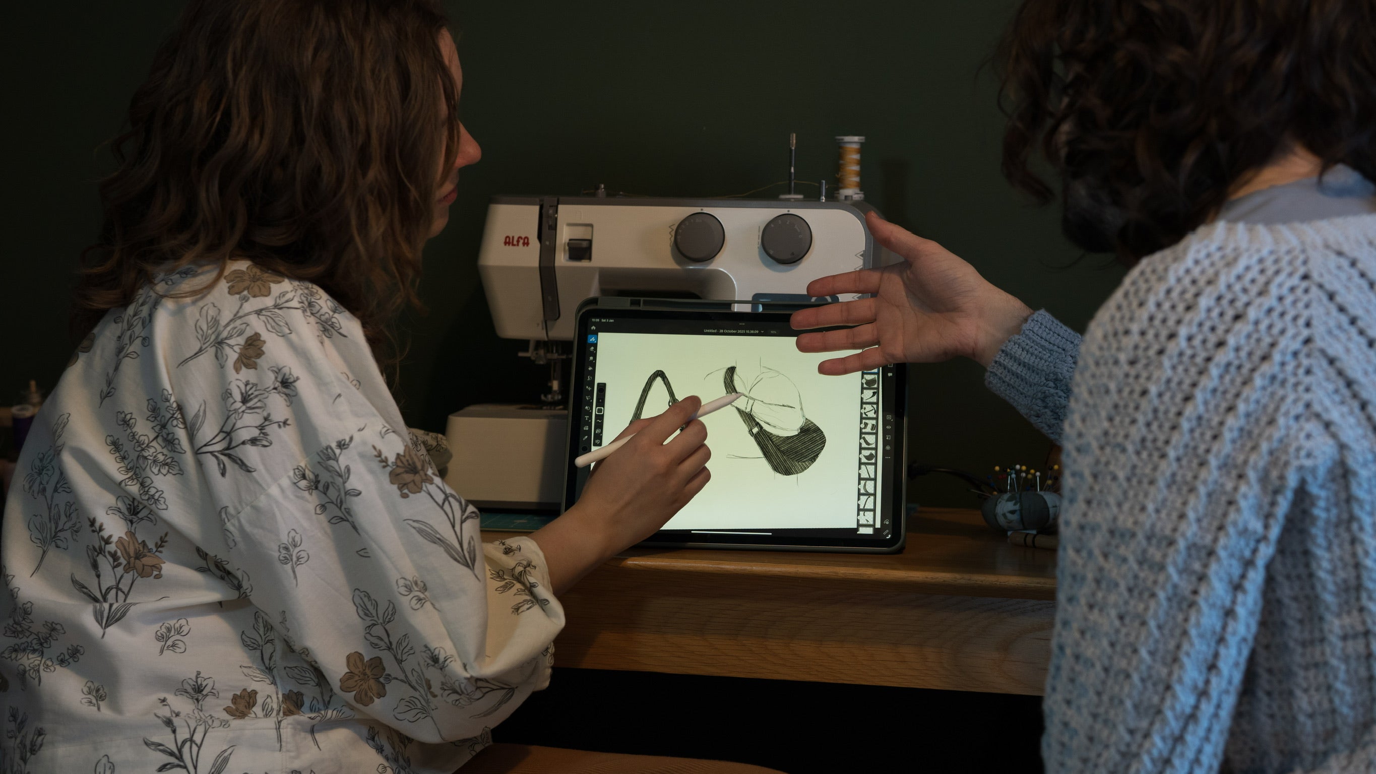 Two people examining an image of a bag on an iPad with a sewing machine in the background