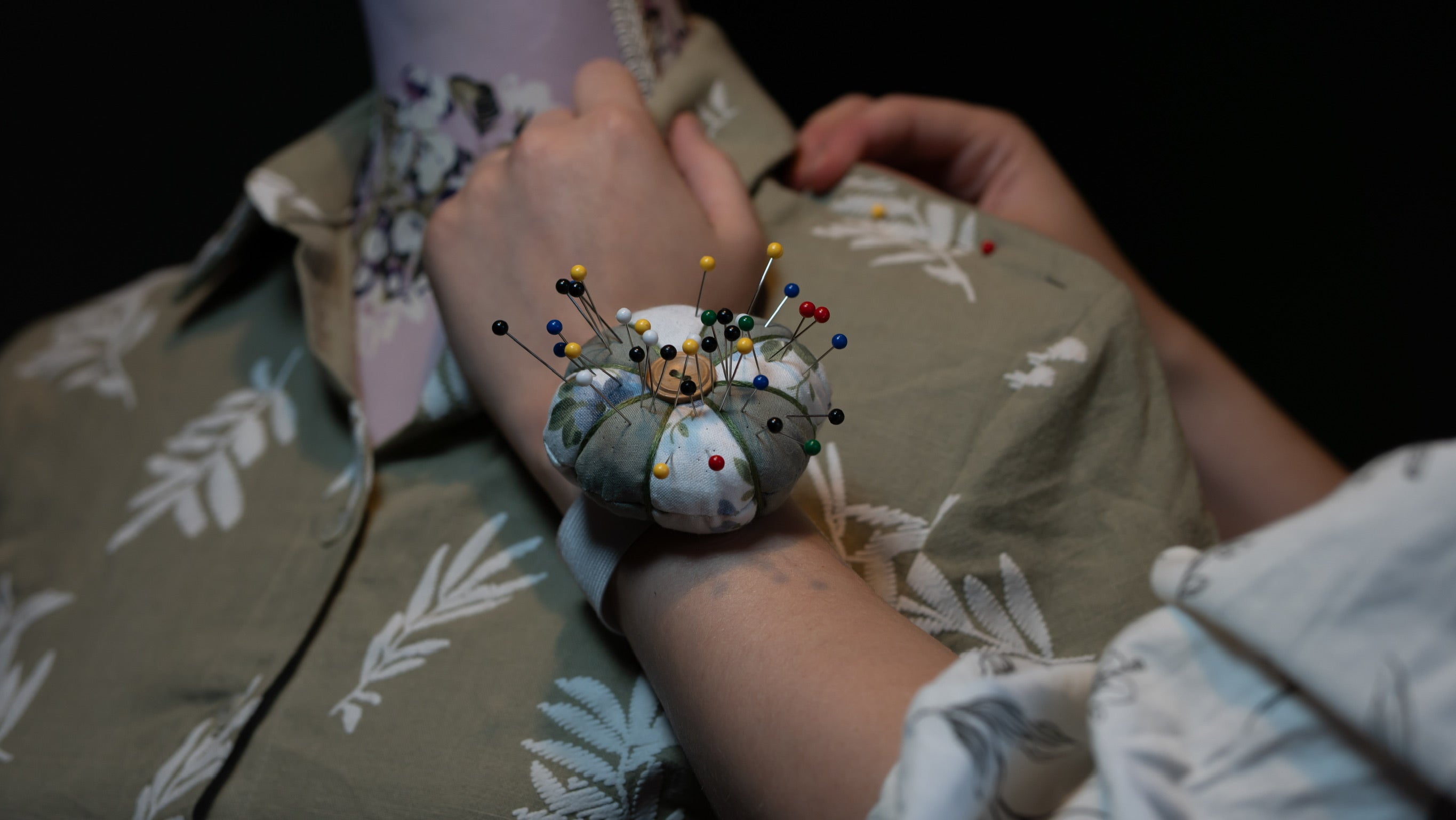 Person wearing a pincushion with pins over a floral-patterned fabric on a mannequin