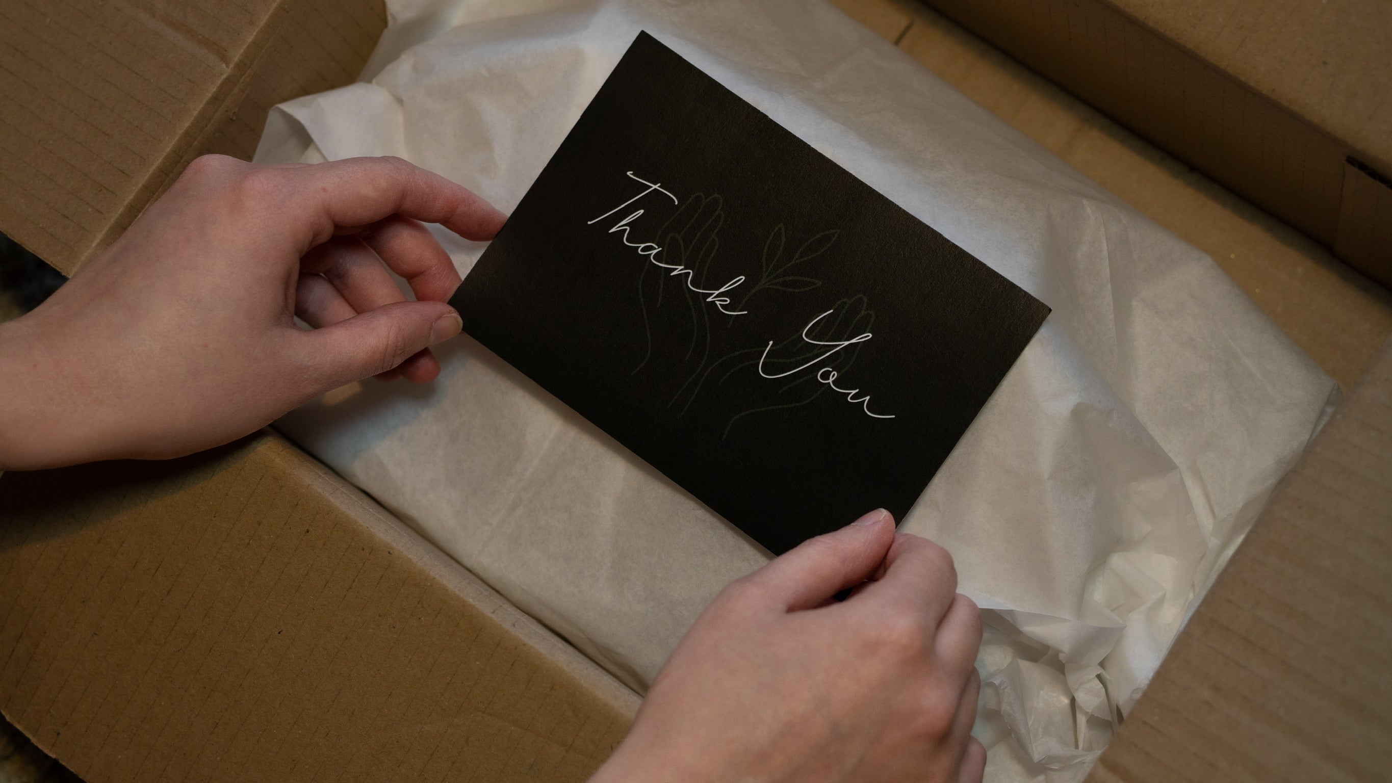 Person holding a dark green card with 'Thank You' on it inside a box.