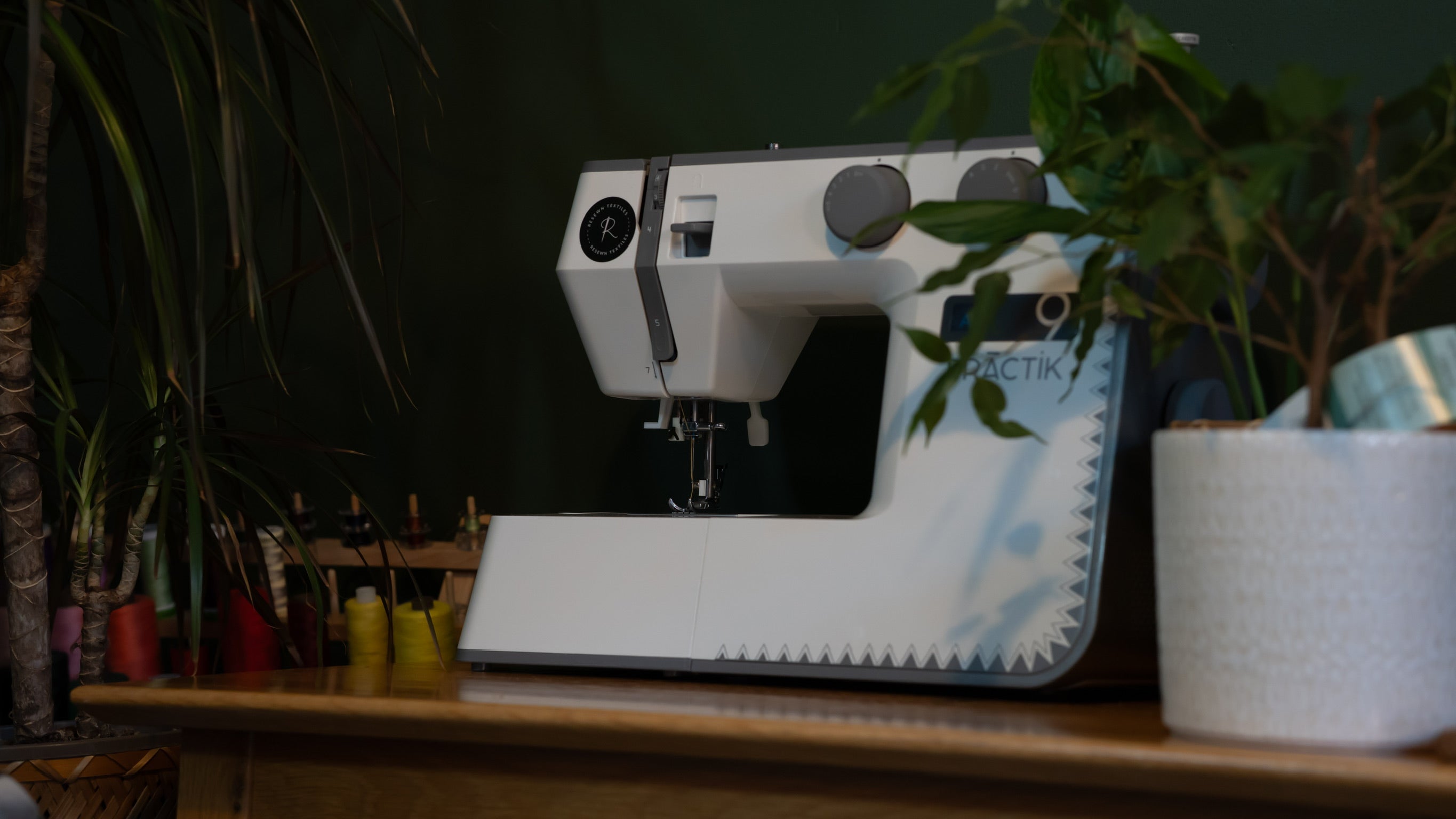 White sewing machine on a wooden surface with plants in the background