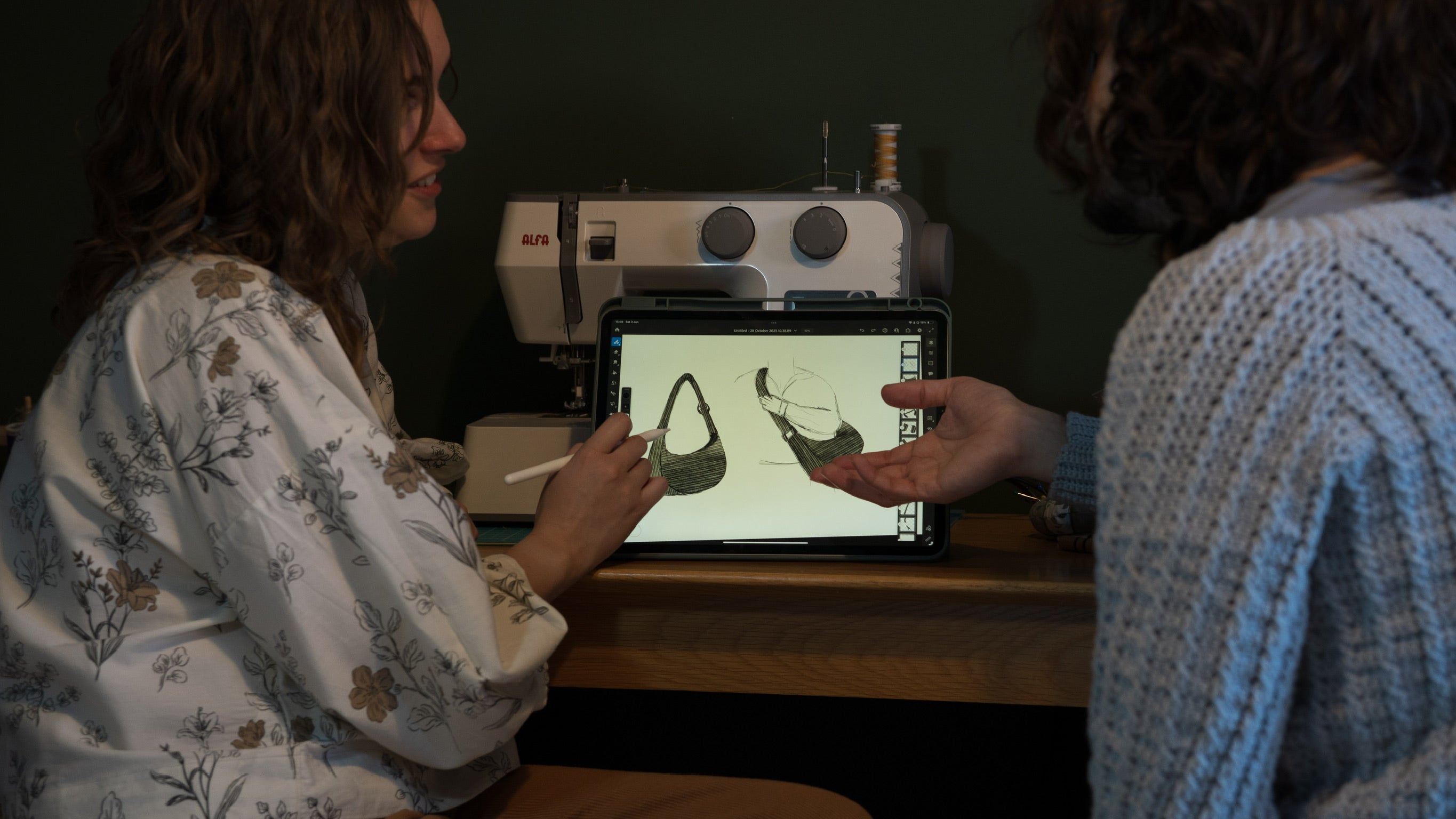 Two people looking at an iPad with a picture of a bag on it with a sewing machine in the background