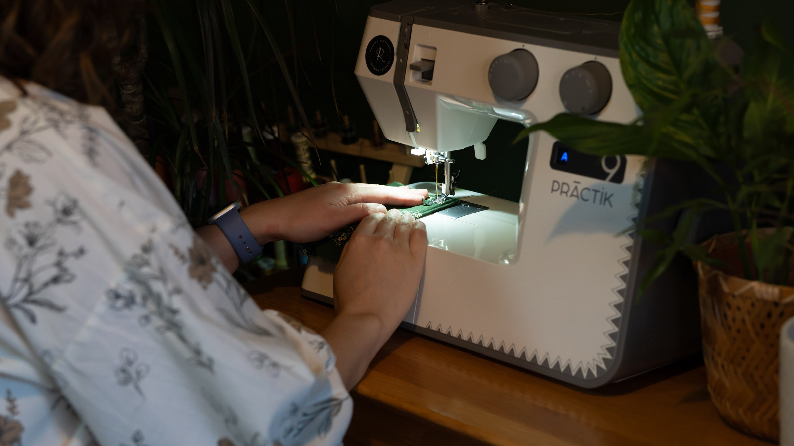 Person using a sewing machine with a plant in the background