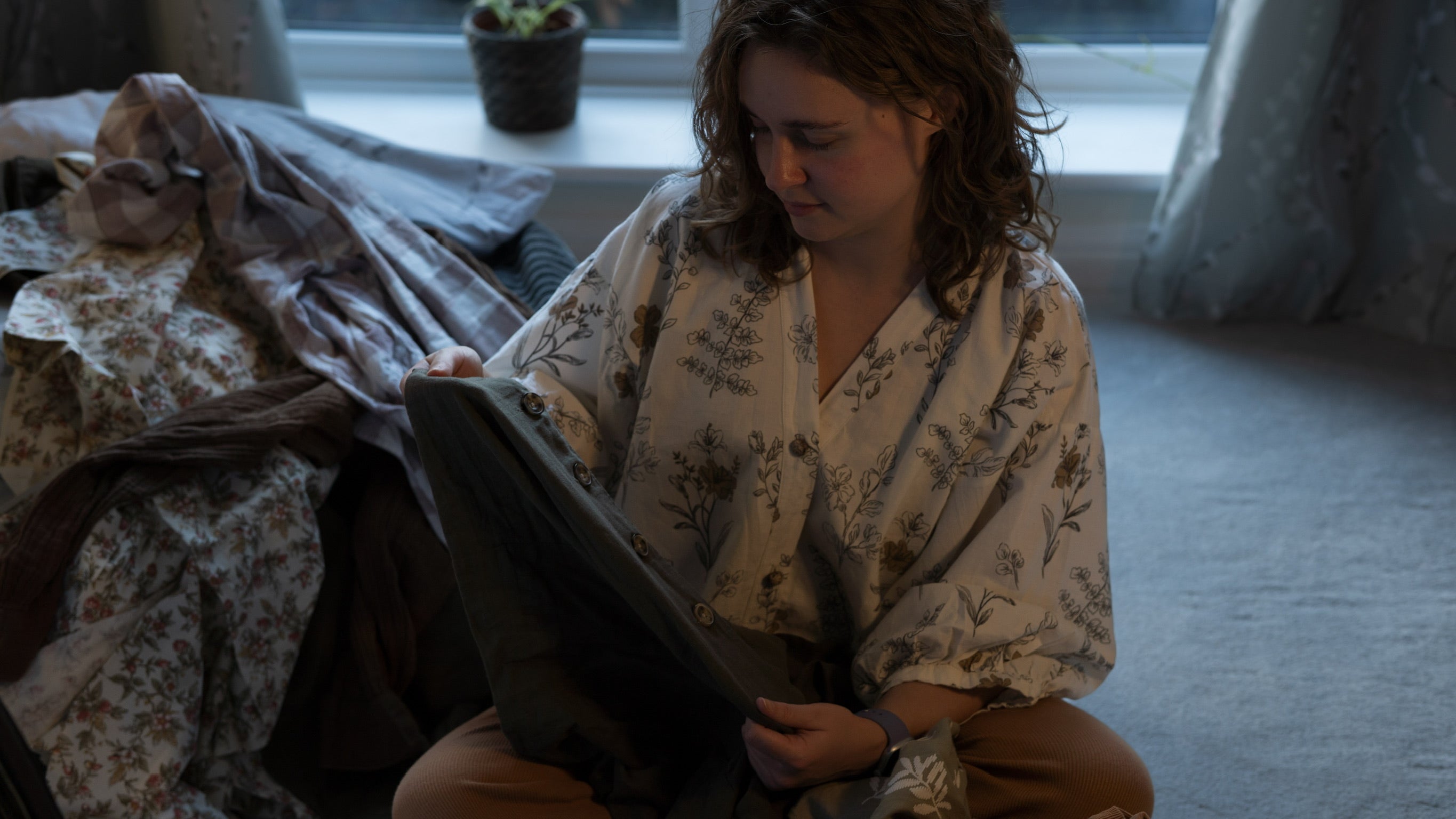 Person sitting on the floor examining an item of clothing with clothes in the background