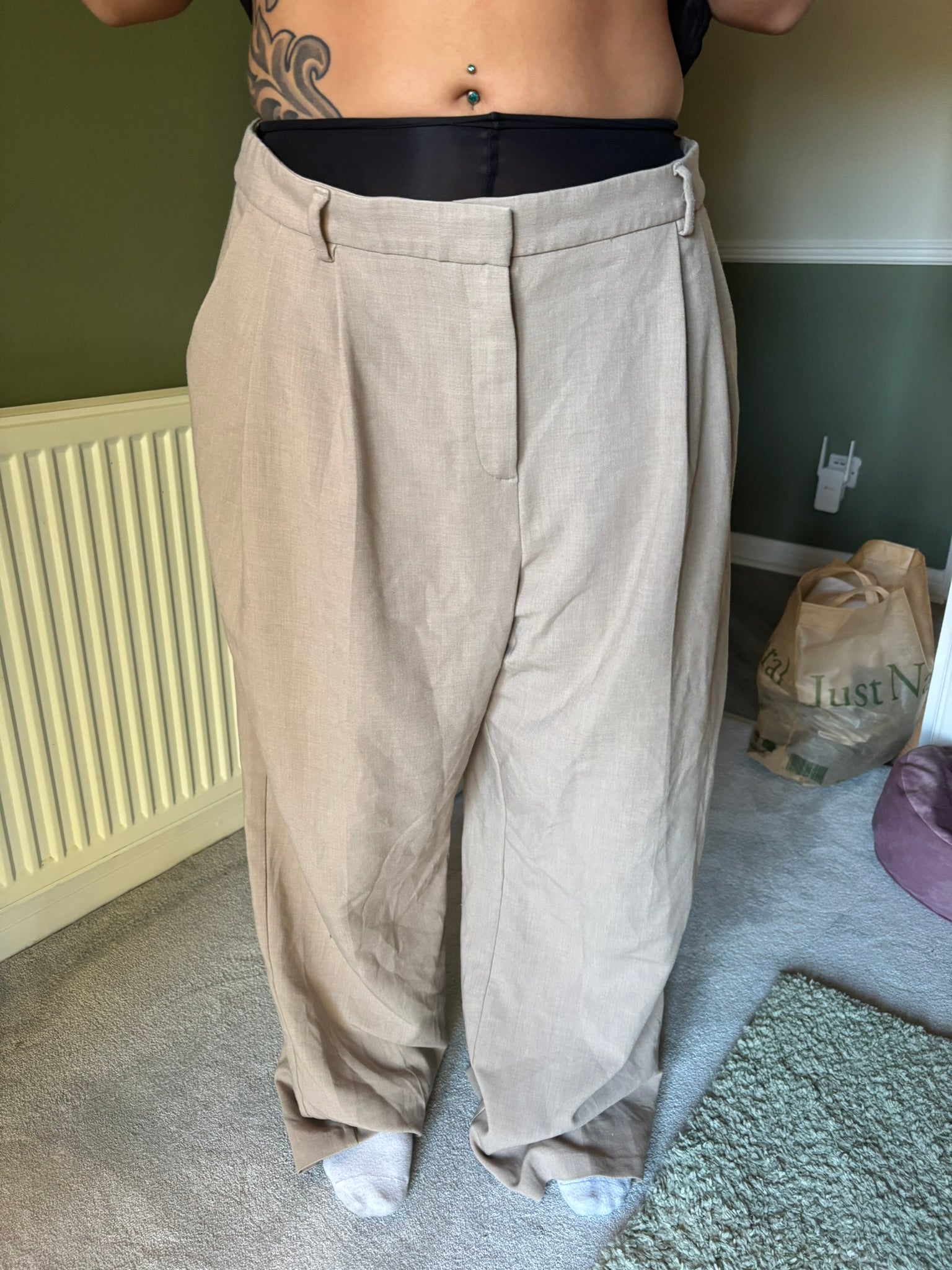 Person wearing beige pants which are too big for them in a room.