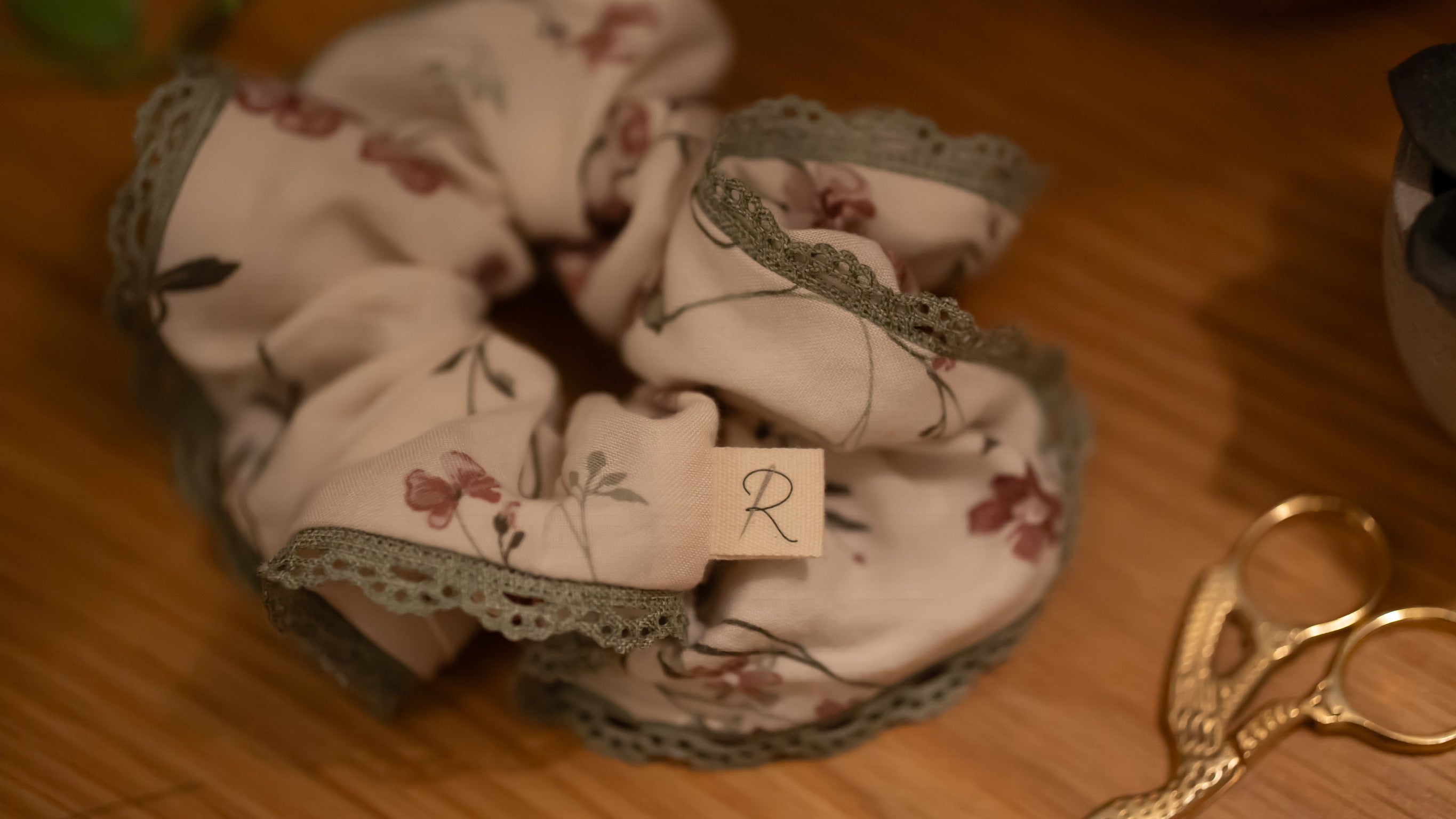 Floral scrunchie with lace trim on a wooden surface next to gold scissors.