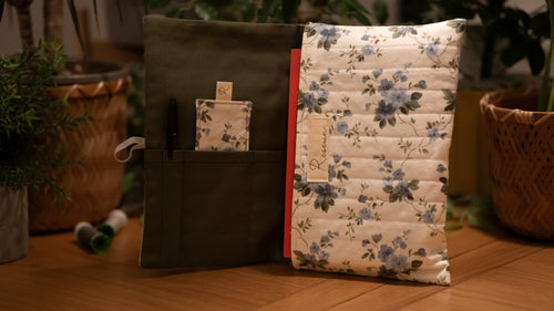 Floral-patterned book sleeve opened to show pockets on a wooden surface with plants in the background