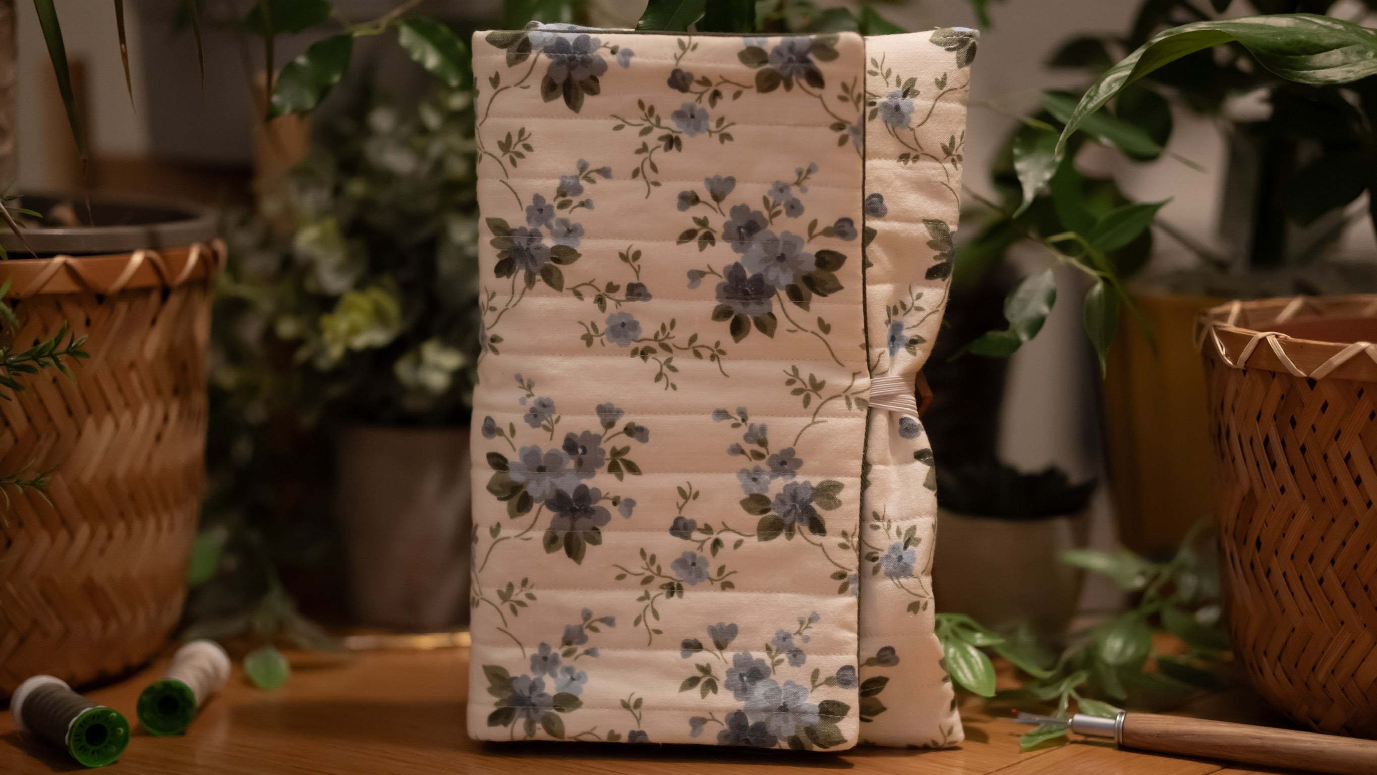 Floral-patterned book sleeve on a wooden surface with plants in the background