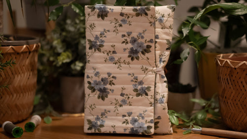 Floral-patterned book sleeve on a wooden surface with plants in the background