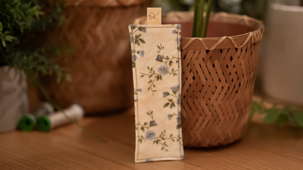 Floral-patterned bookmark on a wooden surface with plants in the background