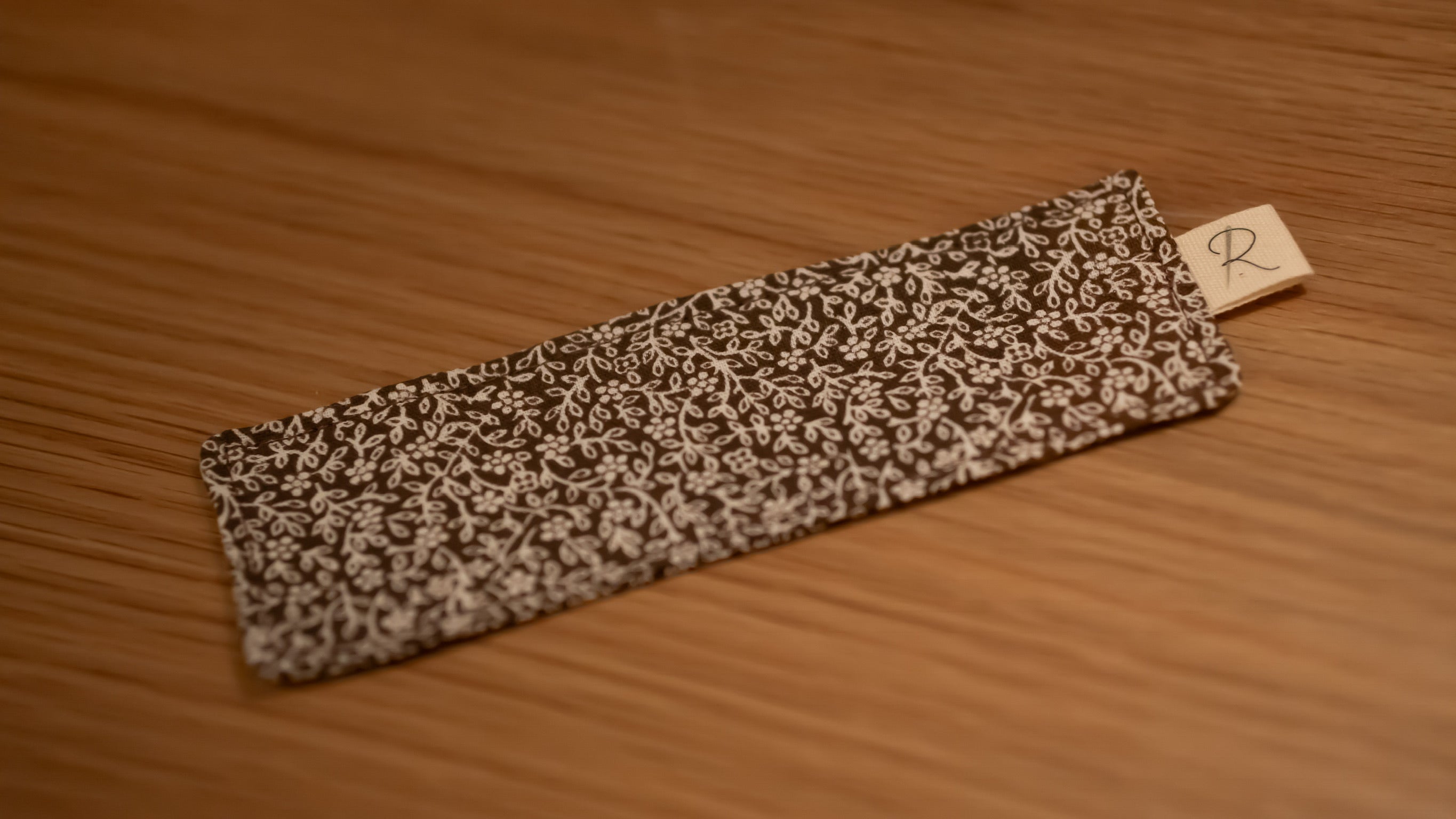 Floral-patterned bookmark on a wooden surface with a visible brand tag.