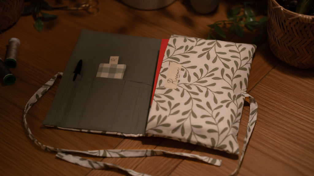 Fabric book sleeve with leaf pattern opened to show pockets on wooden surface