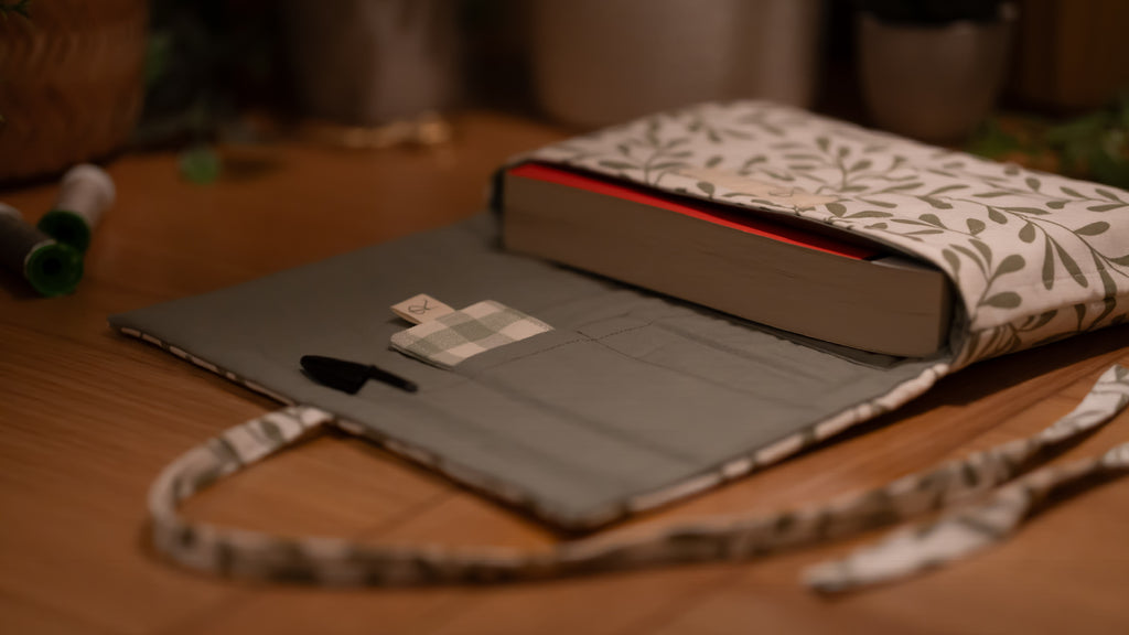 Fabric book sleeve with leaf pattern opened to show pockets on wooden surface