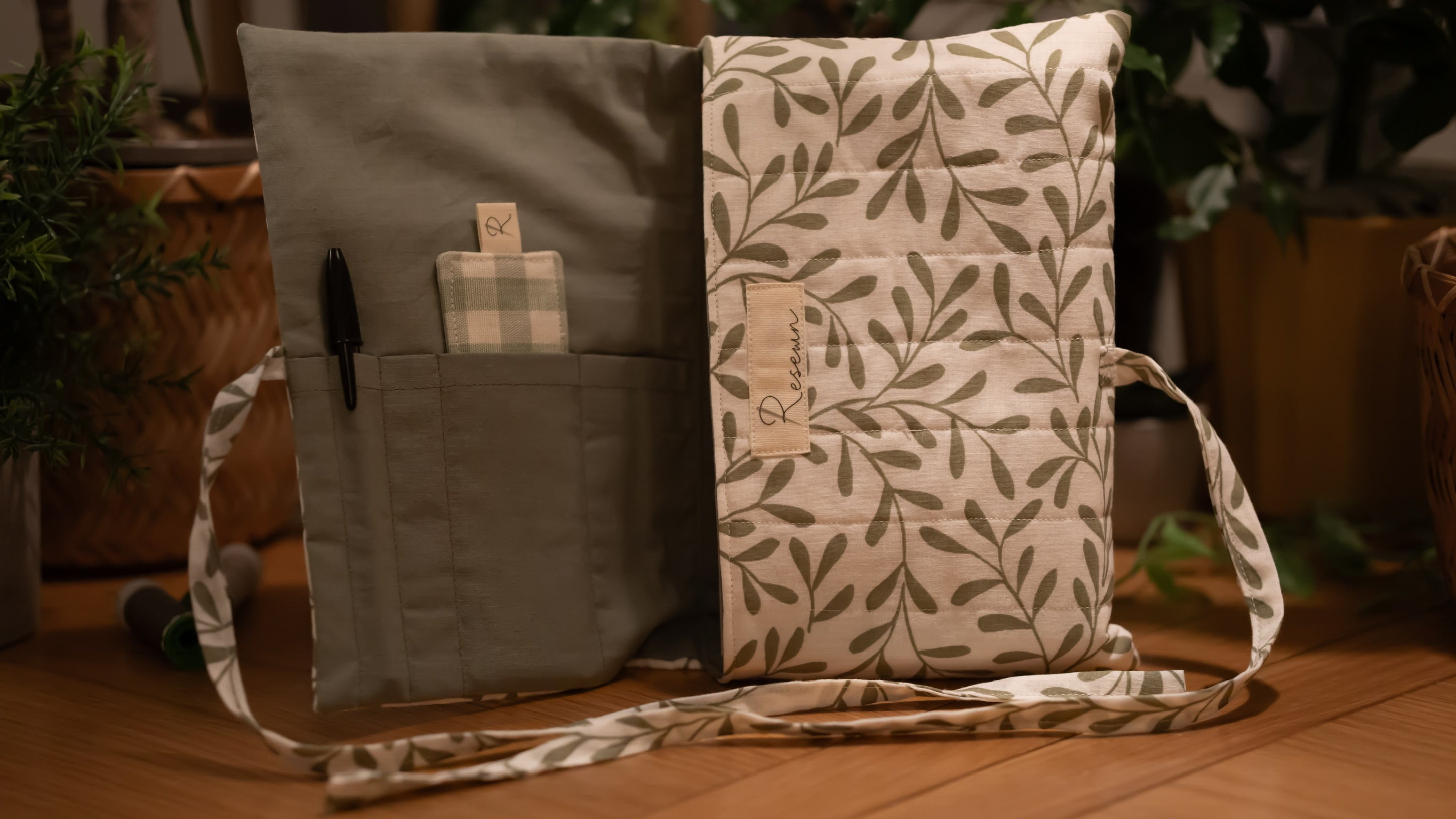 Fabric book sleeve with leaf pattern opened to show pockets on wooden surface