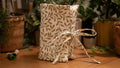 Fabric book sleeve with leaf pattern tied with a string on a wooden surface with plants in the background