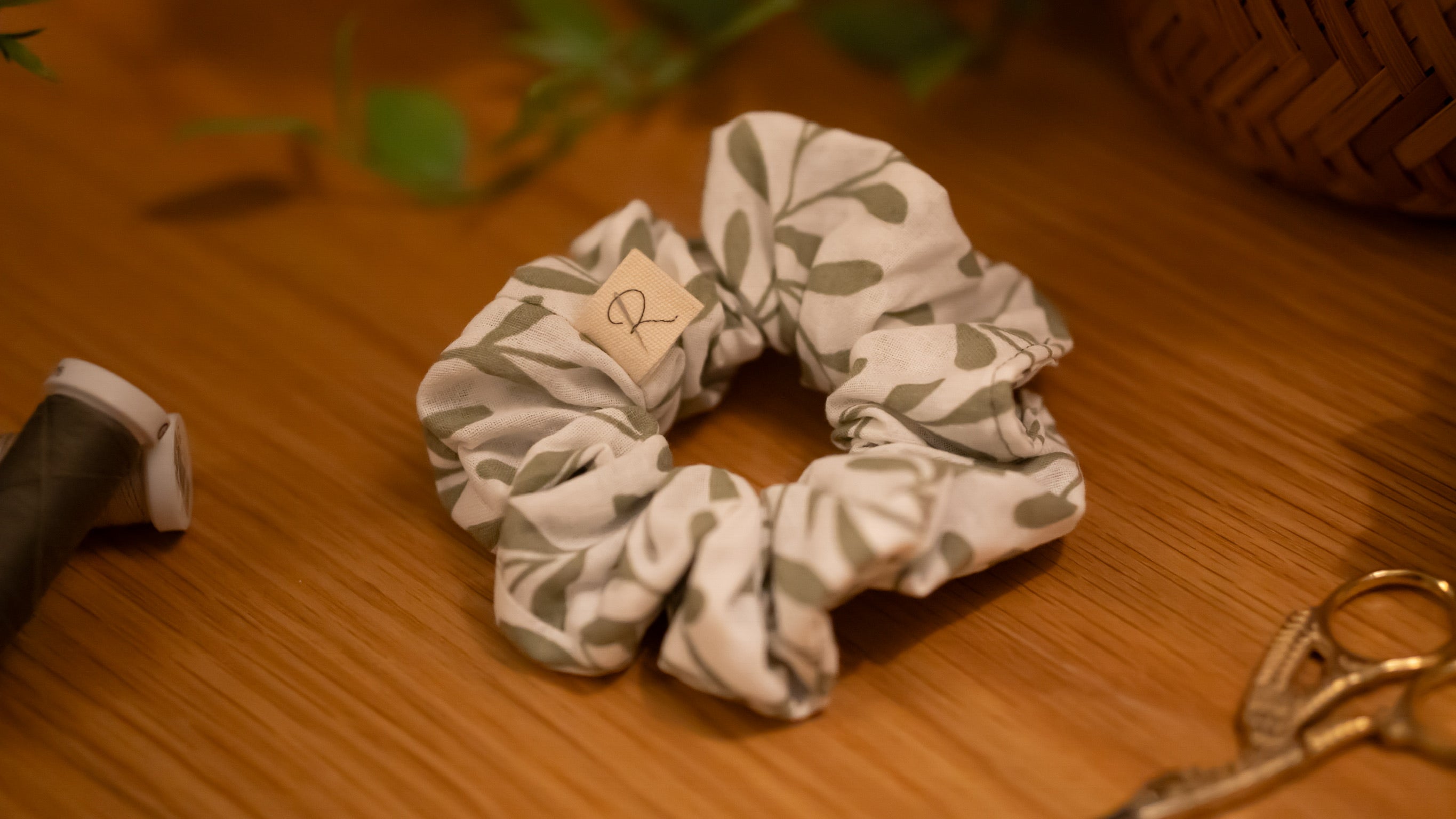 Leaf patterned scrunchie on a wooden surface with scissors and a plant in the background.