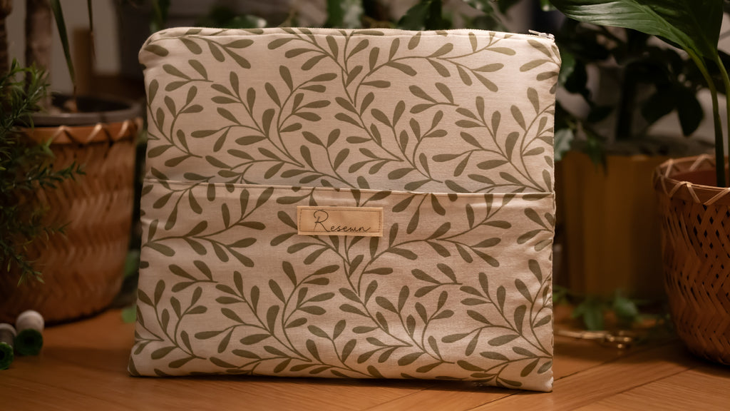Laptop sleeve with leaf pattern and brand label on a wooden surface with plants in the background