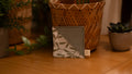 Square bookmark with leaf pattern on a wooden surface surrounded by plants