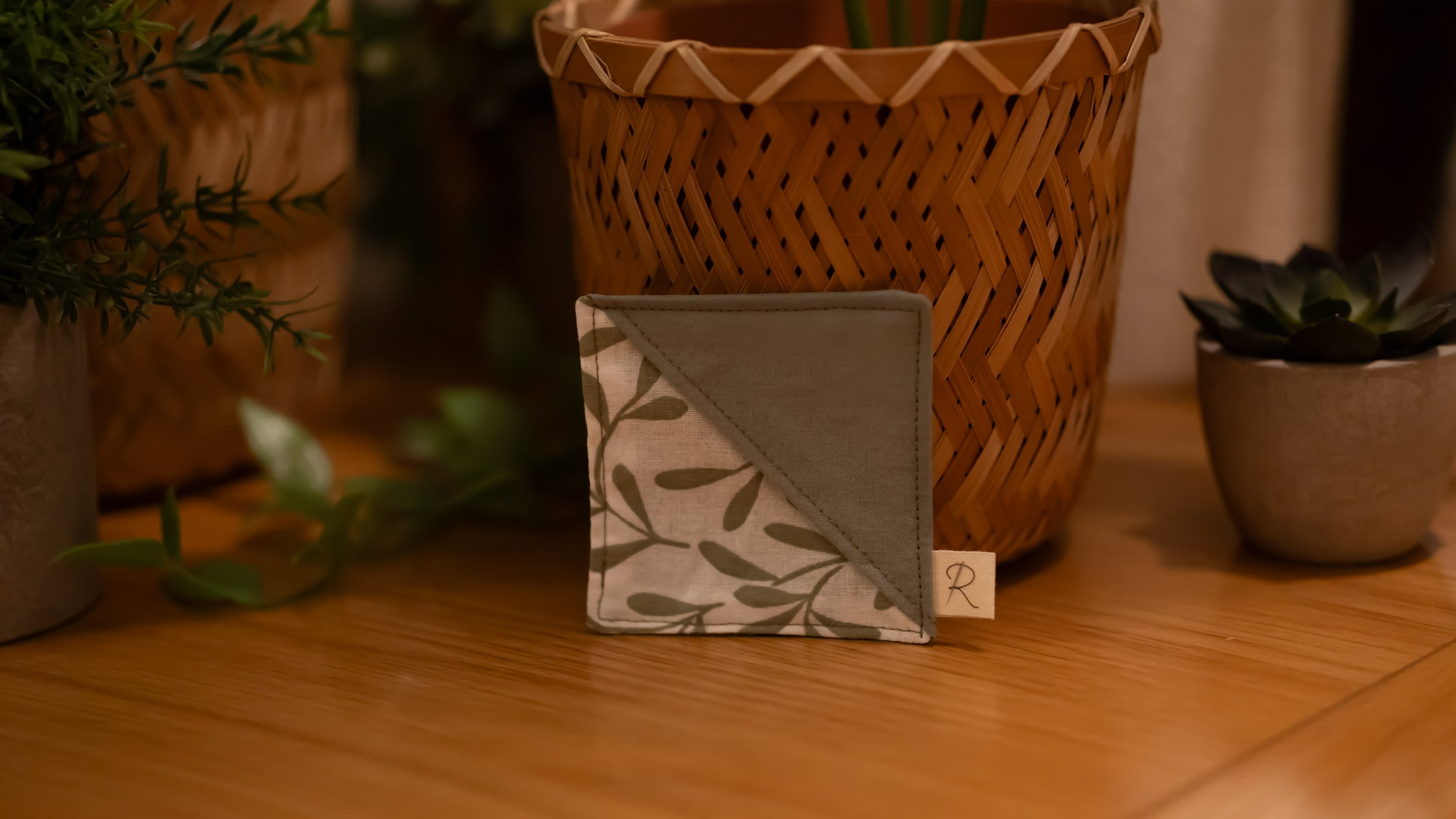 Square bookmark with leaf pattern on a wooden surface surrounded by plants