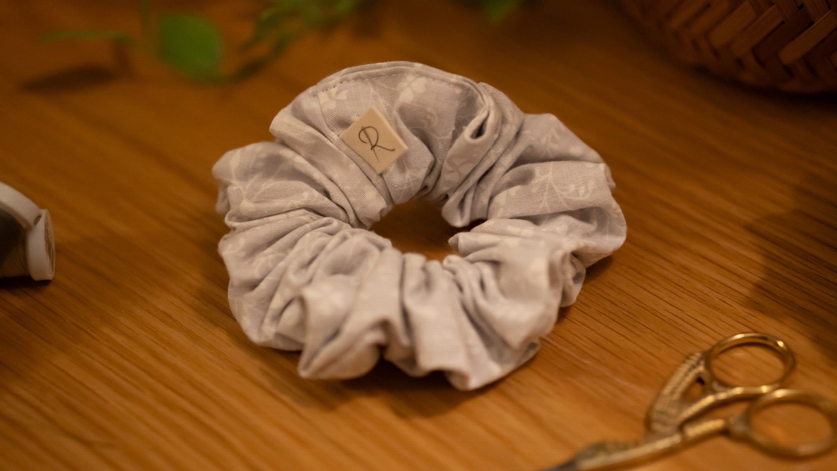 Lilac scrunchie with a brand tag on a wooden surface with scissors in the background