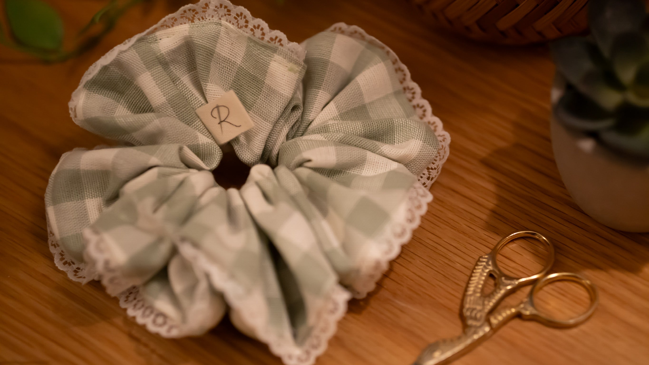 Checkered fabric scrunchie with lace details on a wooden surface with scissors.