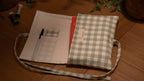 Fabric book sleeve with checkered pattern opened to show pockets on wooden surface