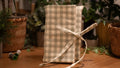 Checkered fabric book sleeve with a ribbon on a wooden surface with plants in the background