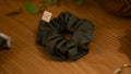 Dark green scrunchie on a wooden surface with a small square tag.