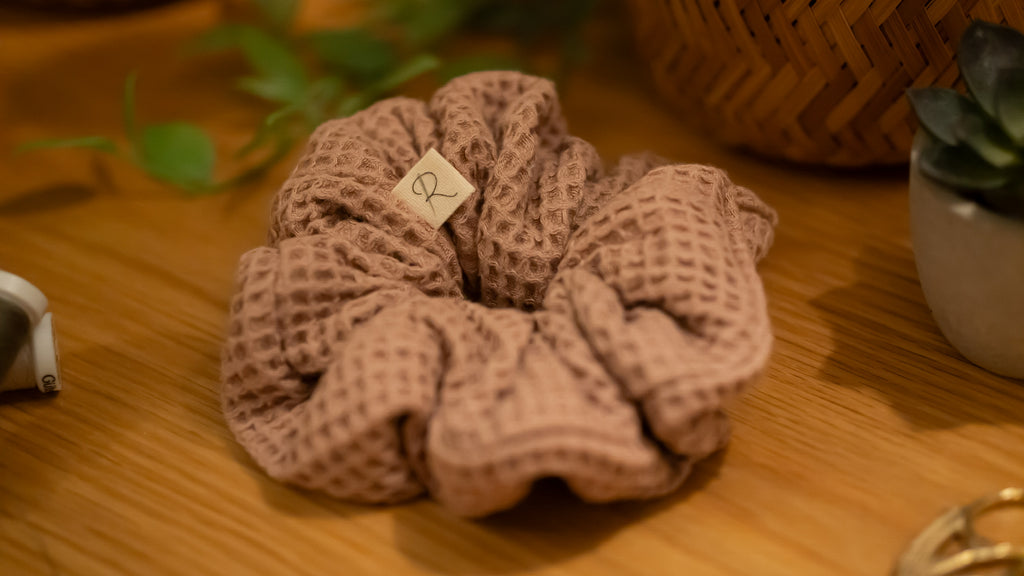 Pink textured scrunchie on a wooden surface with a blurred background