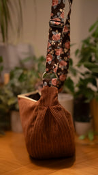 Brown corduroy bag with floral strap on a wooden surface with plants in the background