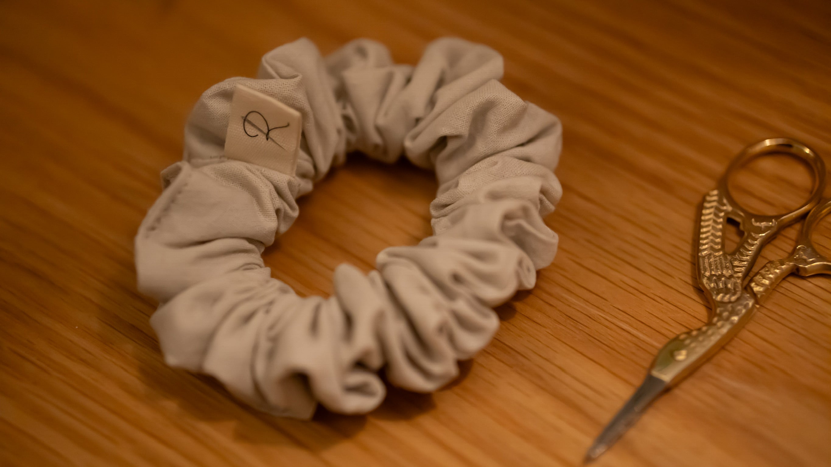 Beige scrunchie with a small square tag and gold scissors on a wooden surface