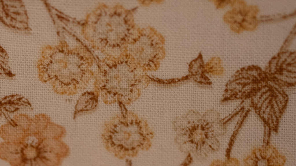 Close-up of floral patterned fabric with brown orange flowers on a beige background