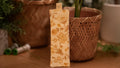 Rectangular fabric bookmark with floral patterns on a wooden surface with plants in the background