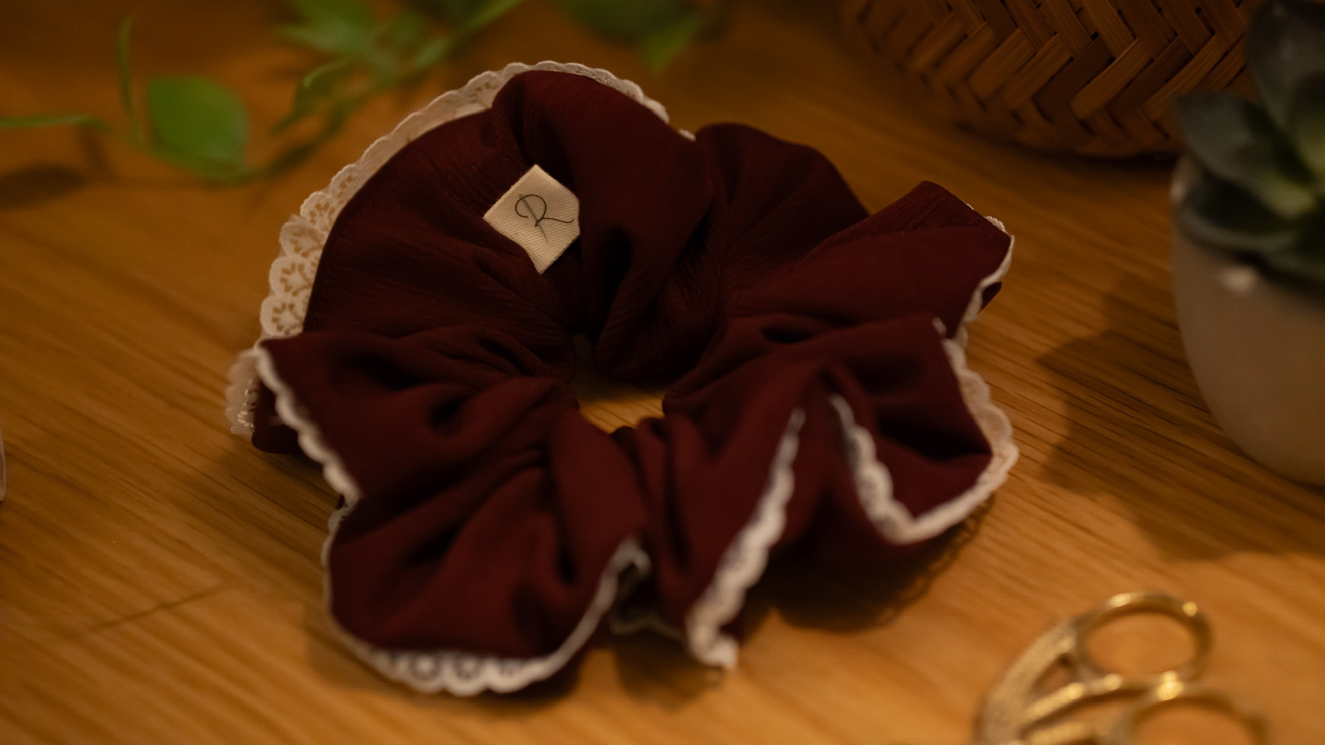 Burgundy scrunchie with lace trim on a wooden surface